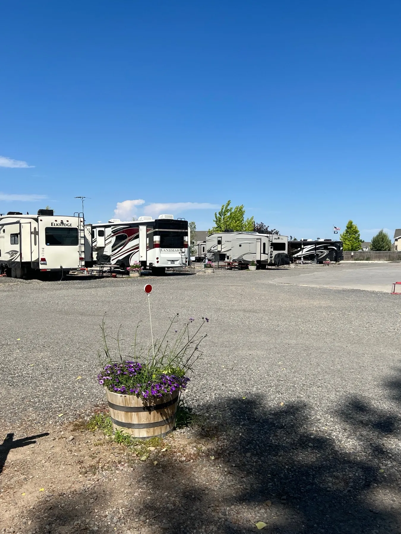 A long gravel pull-through RV row with motorhomes and a flower planter